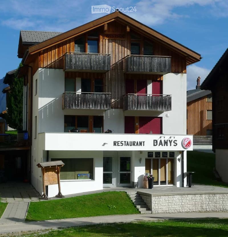 A multi-story building with a restaurant sign reading "RESTAURANT DANY'S" at the base, featuring balconies on the upper floors and a well-maintained lawn in front.