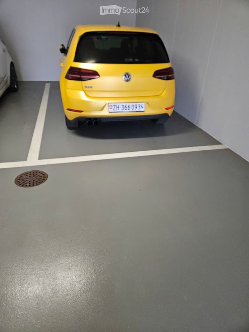 Underground parking space with a yellow Volkswagen car parked in a designated spot, gray concrete floor, and white parking lines.