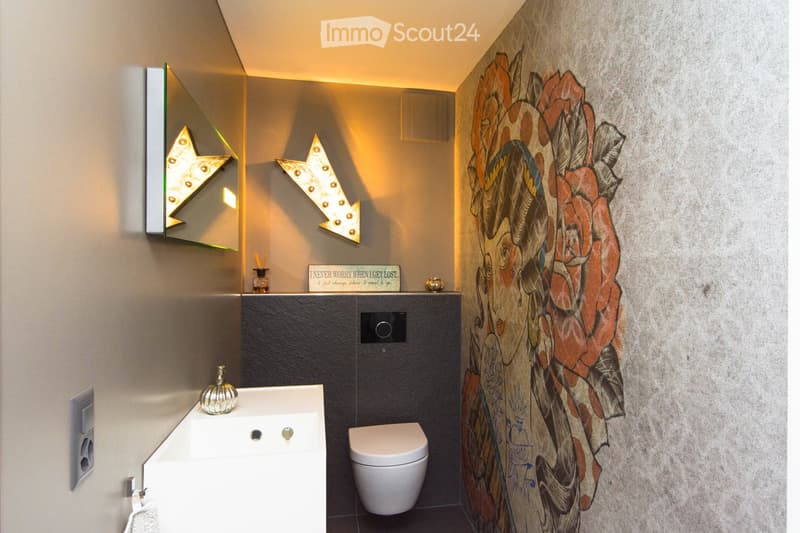 Modern bathroom with a white sink, toilet, decorative wall art, and stylish lighting fixtures.