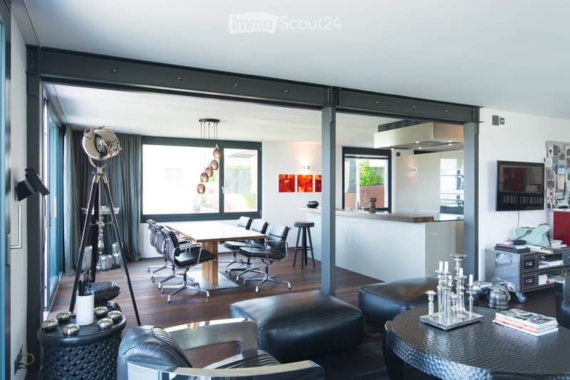 Modern living and dining area with large windows, leather sofa, dining table with chairs, kitchen counter, and decorative items.