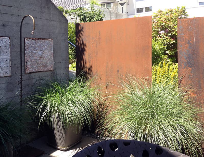 Garden area with tall grasses in pots, decorative metal wall, and modern outdoor furniture.