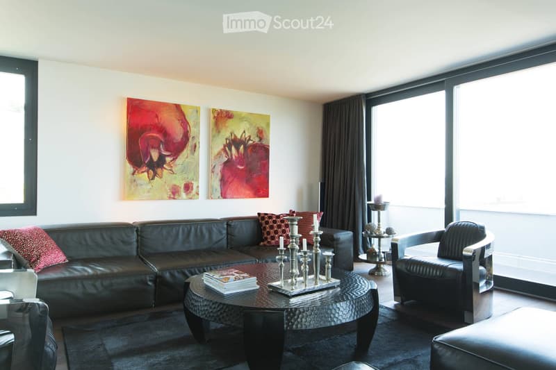 Modern living room with large windows, leather sofa, coffee table, decorative candle holder, and artwork on the walls.