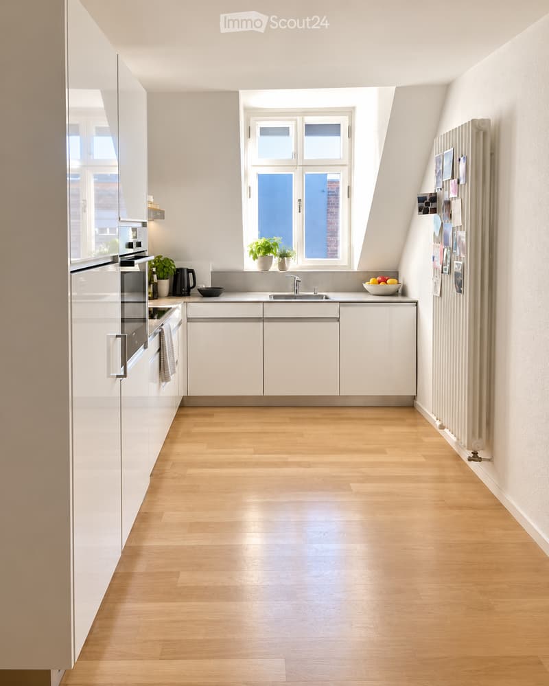 Modern kitchen with white cabinets, wooden flooring, and a large window. Features include a refrigerator, oven, sink, and potted plants on the windowsill.