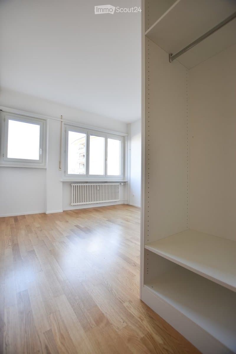 Empty room with wooden flooring, white walls, large windows, and a built-in closet with empty shelves.