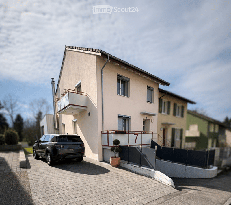Two-story house with beige facade, white trim, balcony, and parked SUV in driveway.
