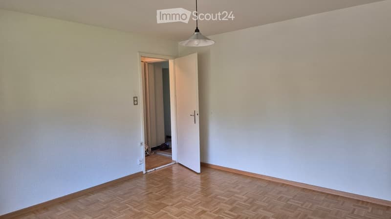 Empty room with light-colored walls, wooden floor, and a single open door leading to another space.
