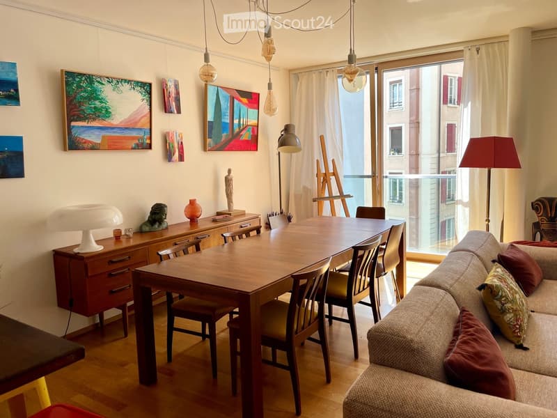 A well-lit living and dining area with a sofa, dining table, chairs, a wooden cabinet, and various decorative items including paintings and sculptures.