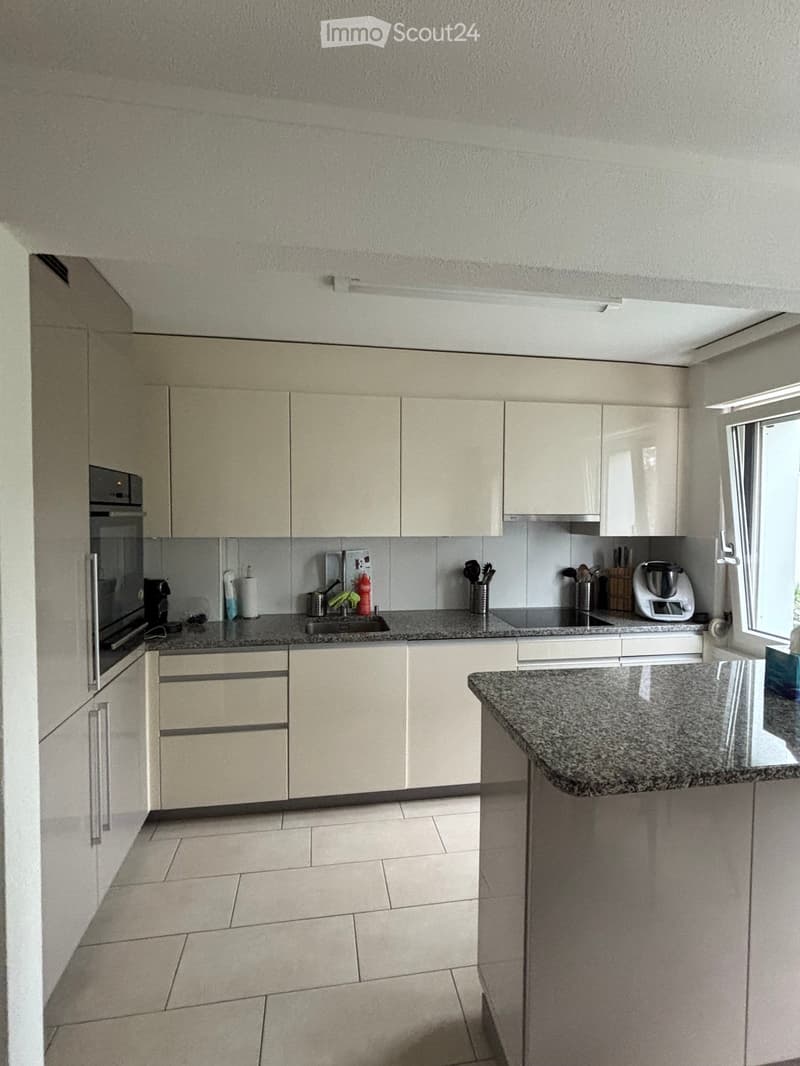 Modern kitchen with light-colored cabinets, granite countertop, and various appliances including an oven, sink, and blender.