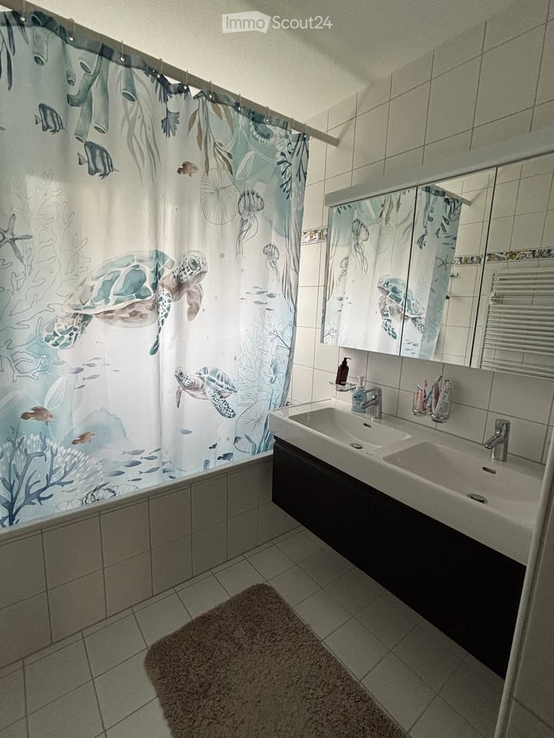 Modern bathroom with a double sink vanity, a large mirror, and a shower with a decorative ocean-themed curtain featuring turtles and fish.