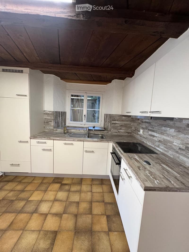Modern kitchen with white cabinets, wooden countertop, tiled floor, and stainless steel sink and oven.