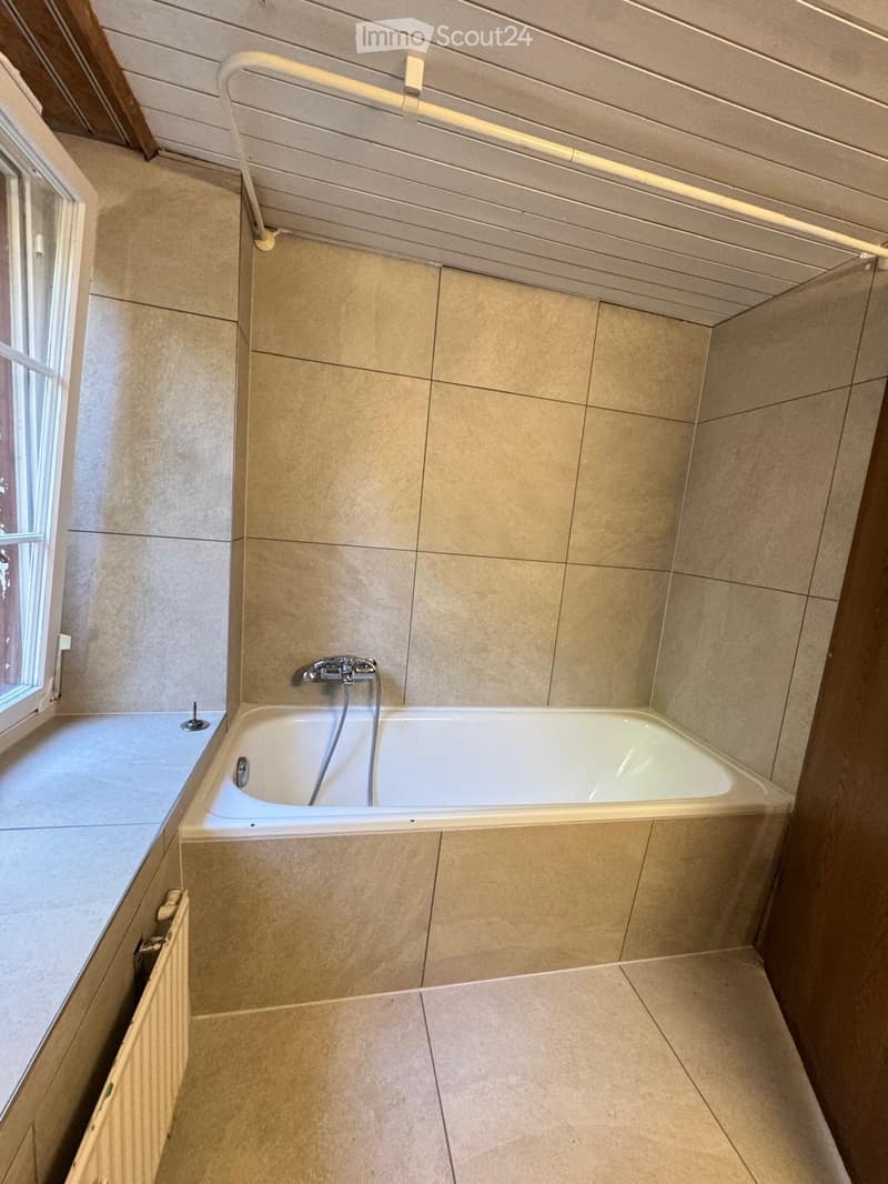 Bathroom with a bathtub, tiled walls and floor, a window, a radiator, and a safety grab bar.