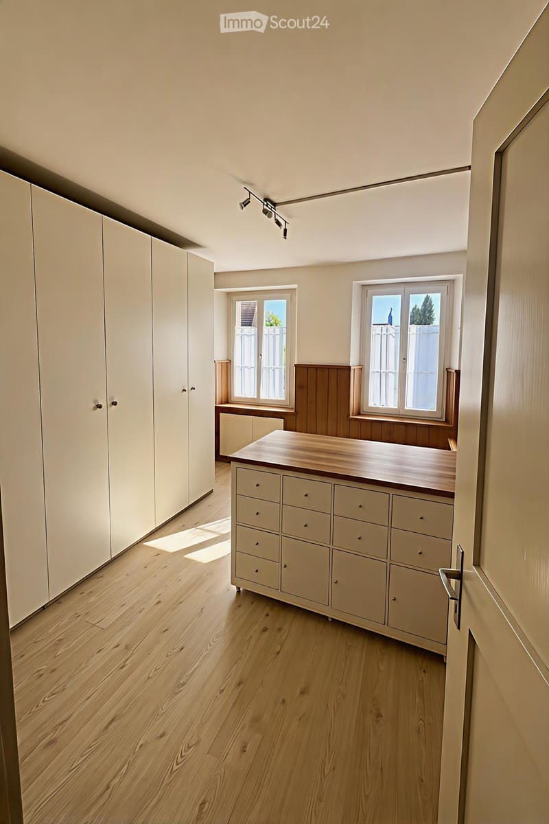 Bright, minimalist kitchen with light wooden flooring, white cabinets, and a central kitchen island with drawers.