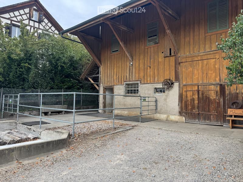 Two-story wooden building with a barn-like structure, metal fence, and small wooden bench.