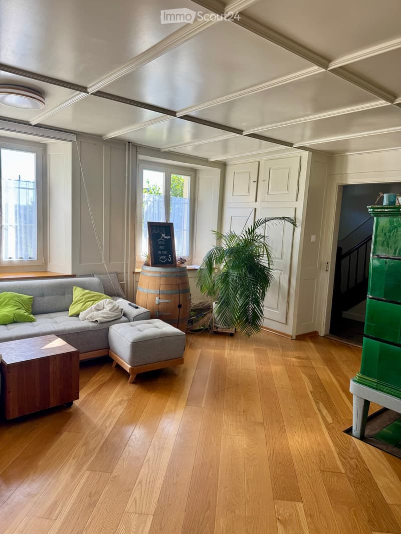 Living room with wooden flooring, grey sectional sofa, ottoman, coffee table, barrel, and potted plant.