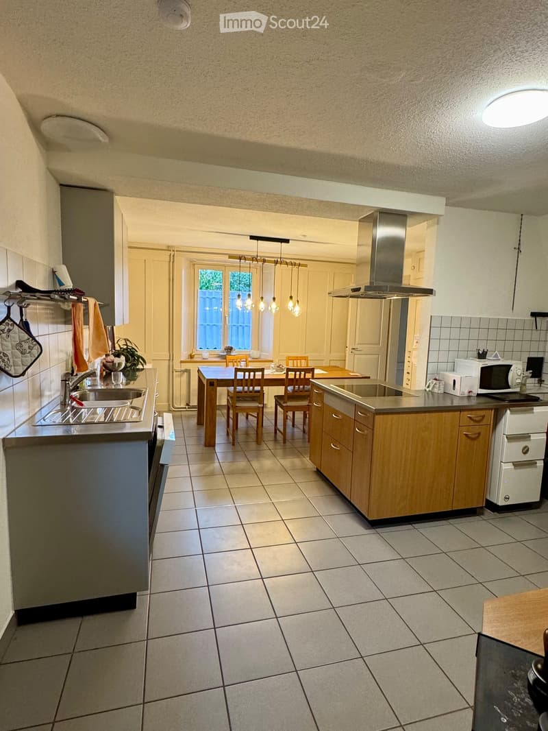 Modern kitchen with tiled floor, wooden cabinets, stainless steel appliances, and a dining area with a table and chairs.