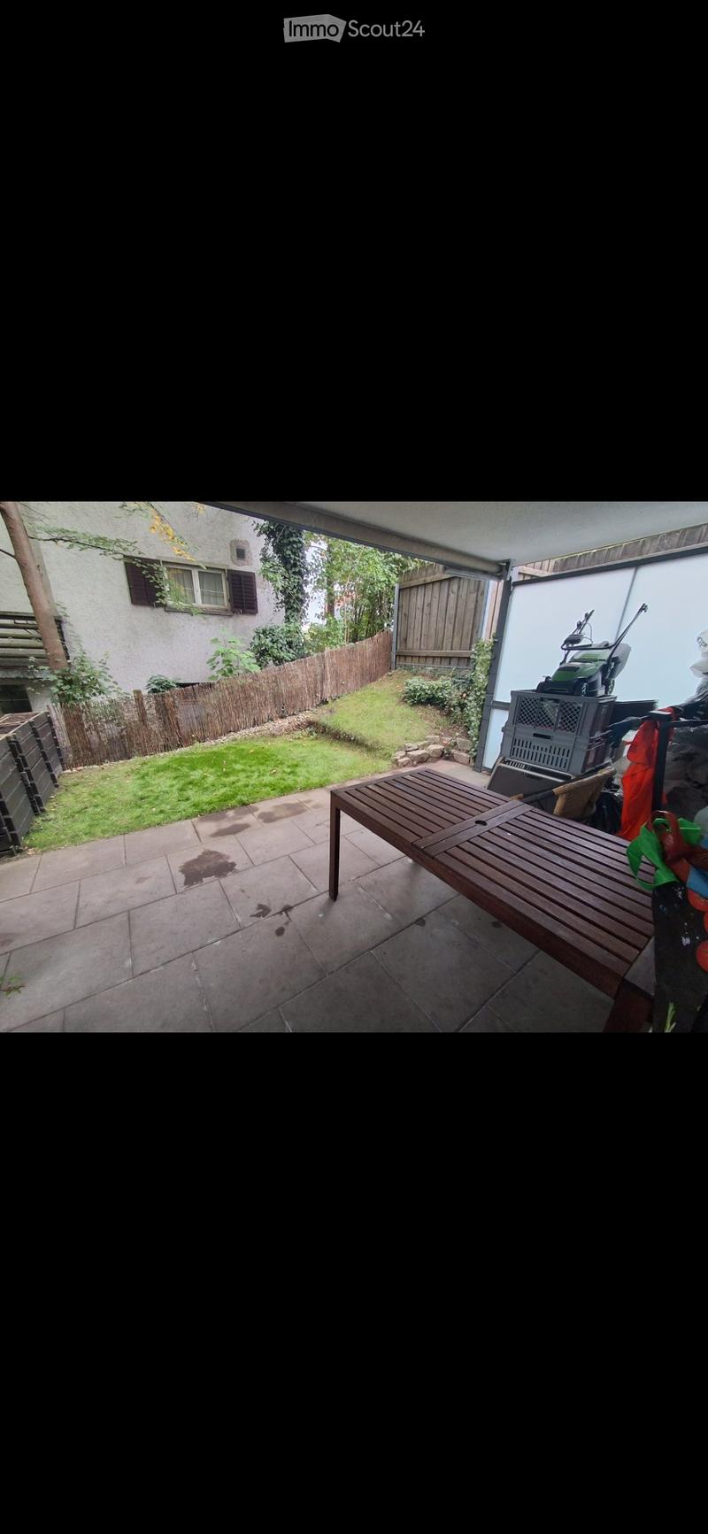 Patio area with tiled floor, wooden bench, grassy lawn, wooden fence, and neighboring house visible.