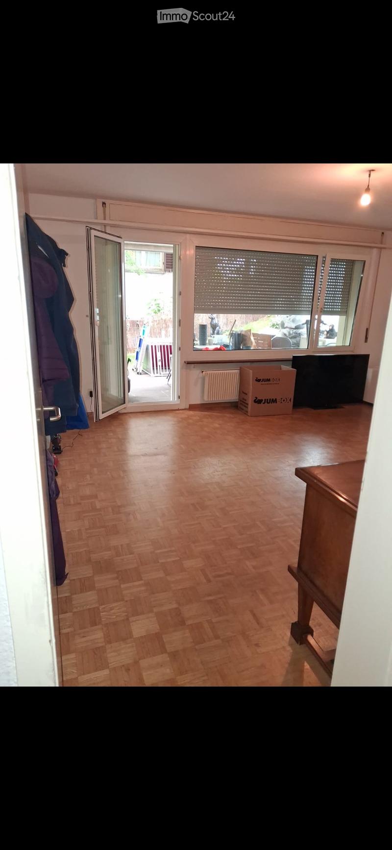 Empty room with wooden flooring, large windows with blinds, and an open sliding door leading to a patio area.
