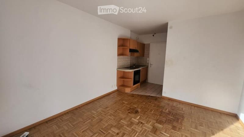 Empty room with wooden flooring and a small kitchen area featuring cabinets, a sink, and an oven.