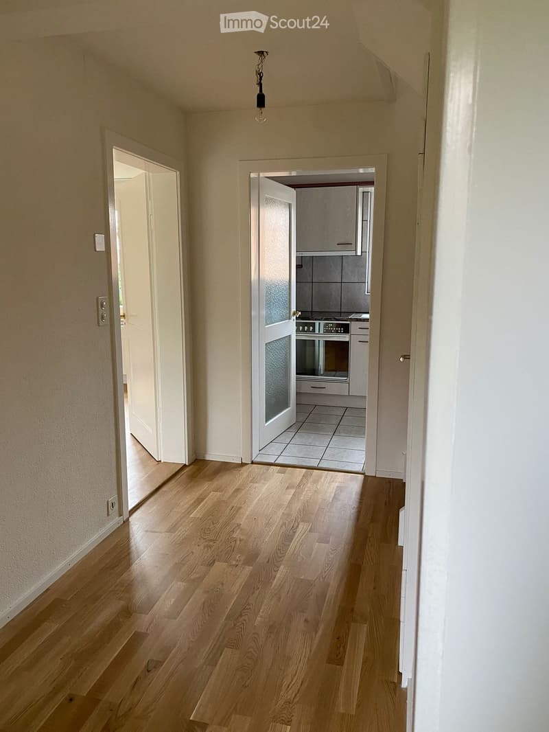 Empty hallway with light wooden flooring, white walls, and two open doors leading to other rooms.