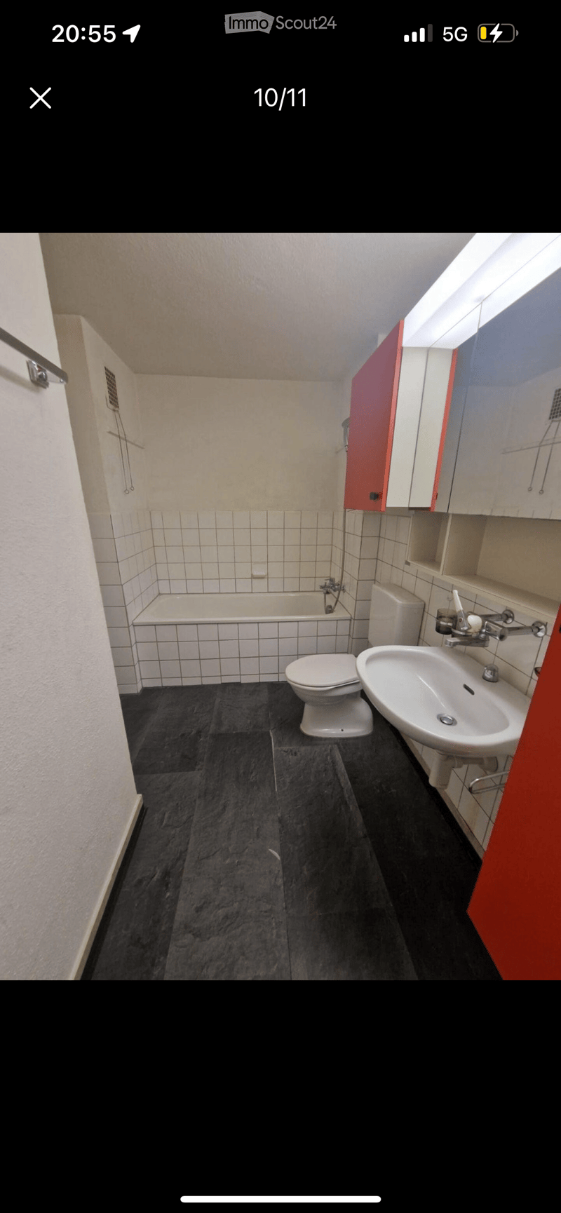 Bathroom features a bathtub, toilet, and sink with cabinets, white tiled walls and floors, red cabinet, and ceiling light.