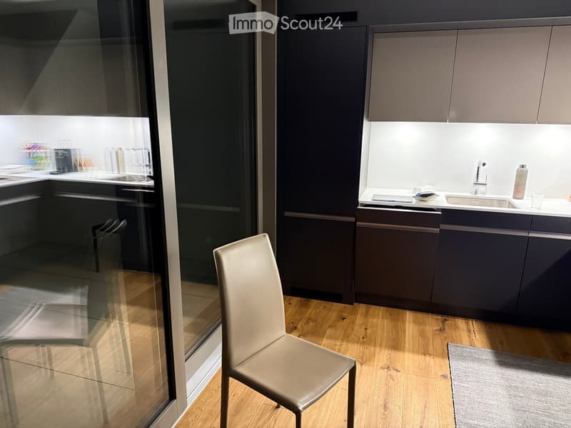 Modern kitchen with dark grey cabinets, a white countertop, a sink, and a single chair near the counter.