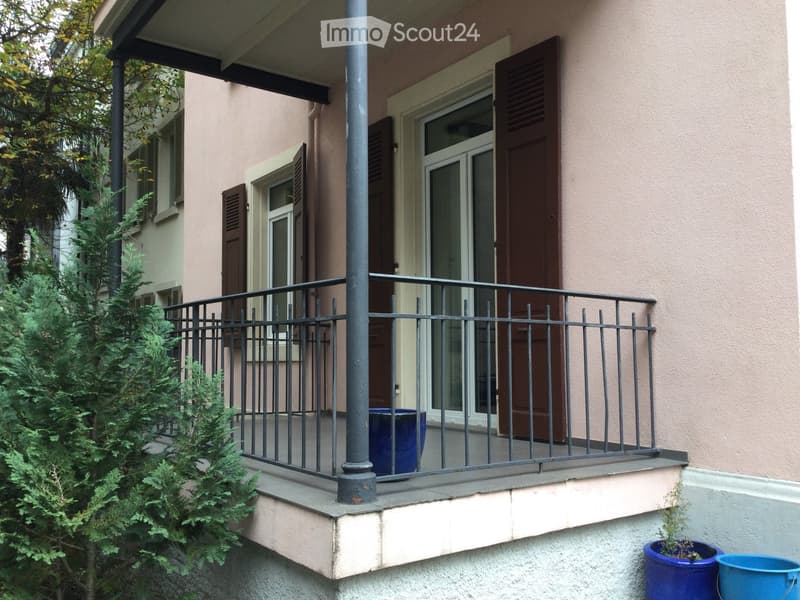 Balcony with black metal railing, beige wall, and two blue pots on the floor.