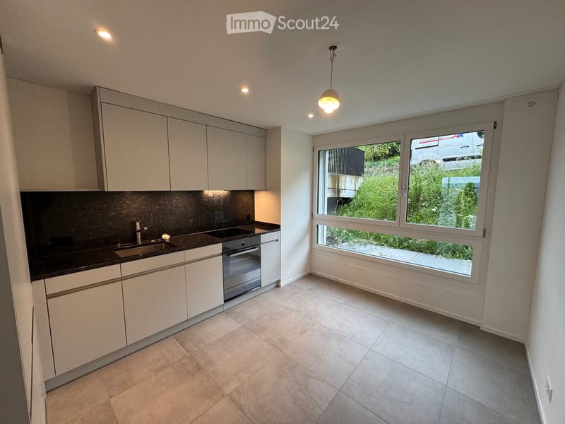 Modern kitchen with white cabinets, black countertop, stainless steel sink, and built-in oven. Large window offers a view of greenery outside.