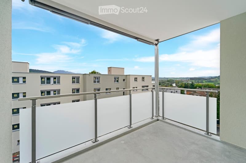 Balcony with white privacy screens, metal railing, and a view of a multi-story building and distant landscape.