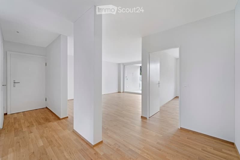 Empty hallway with light wooden flooring, white walls, and white doors. No furniture or equipment present.