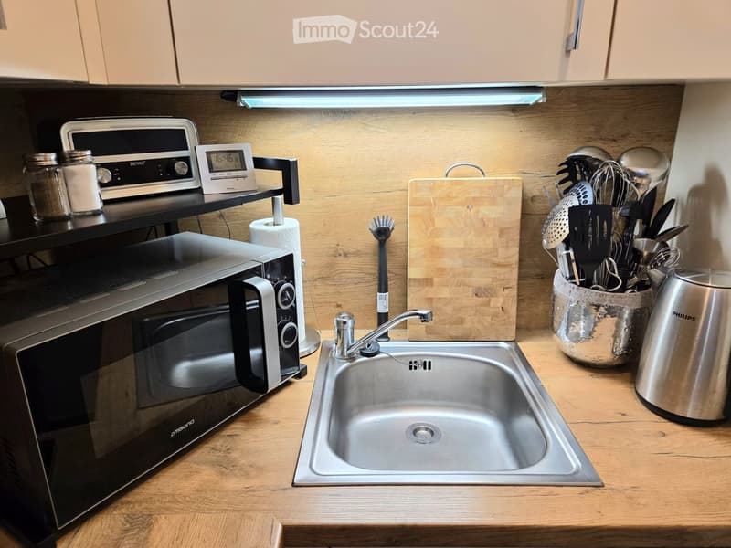 Modern kitchen with wooden countertops, stainless steel sink, microwave, and various kitchen utensils neatly arranged.