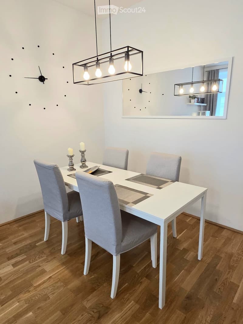 Dining room with a white dining table, four grey upholstered chairs, two candles on the table, and modern light fixtures.