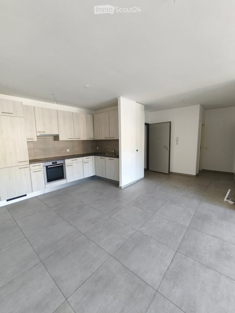 Empty kitchen with light wood cabinets, stainless steel appliances, and tiled floor.
