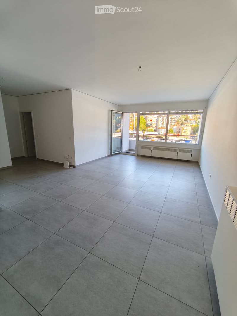 Empty room with tiled floor, white walls, large windows, and a sliding glass door leading to a balcony.