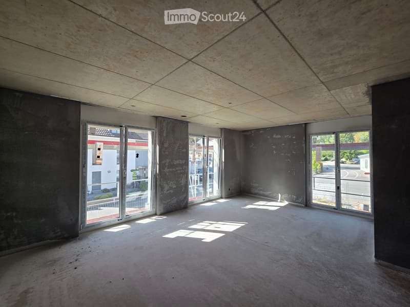 Empty room with concrete walls and ceiling, large windows, and a sliding door leading to an outdoor area.