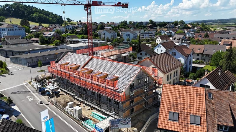 Aerial view of a residential area with a partially constructed building under scaffolding, surrounded by completed houses and greenery.
