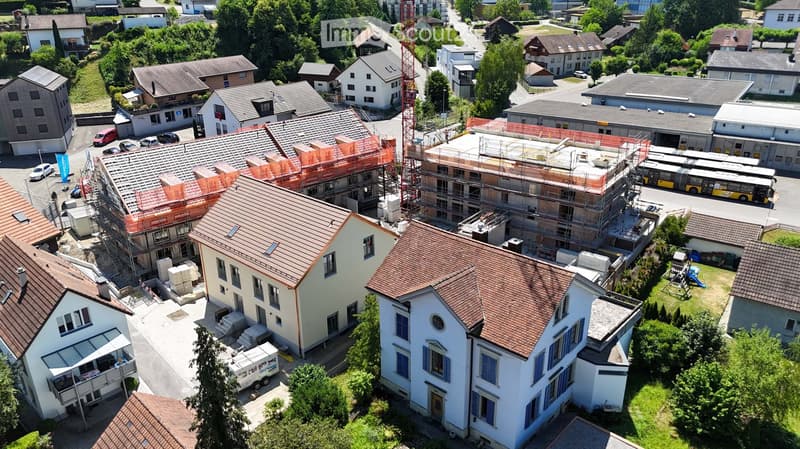Aerial view of a residential area with multiple houses, some under construction, surrounded by greenery and a few parked cars.
