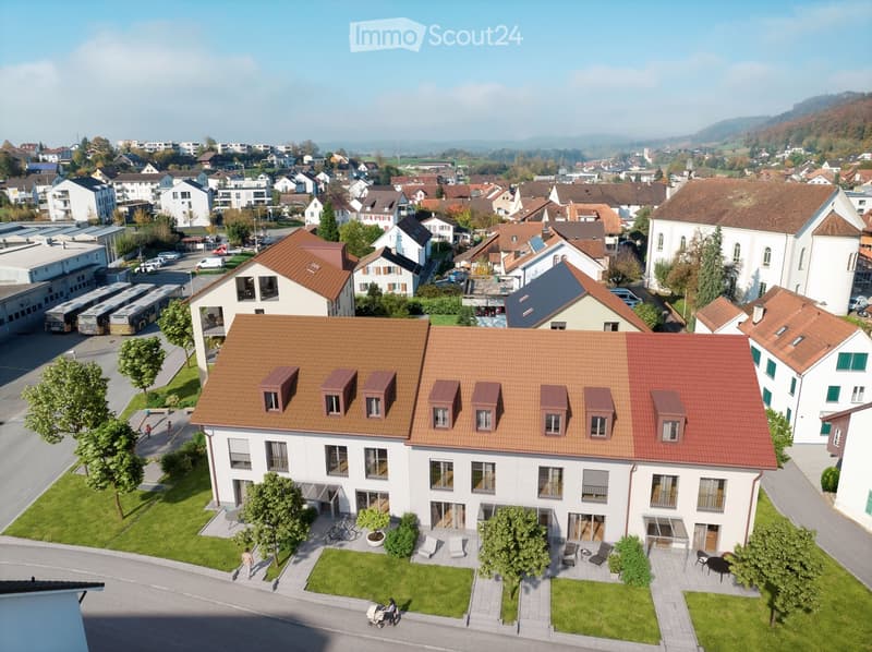 Aerial view of a residential area with a large white building with a brown roof, multiple windows, and a small garden in front.