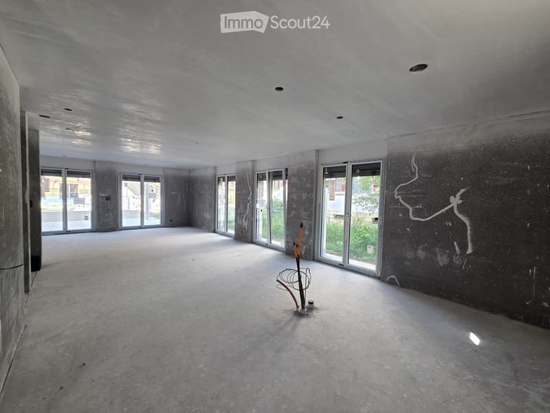 Empty room with concrete floors and walls, large windows, and a small decorative stand in the center.
