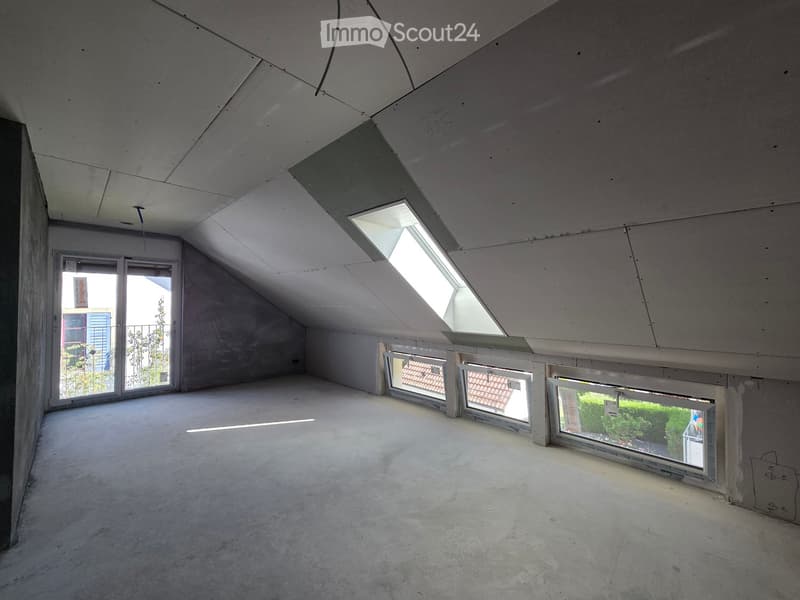 Empty attic space with concrete floors, exposed ceiling beams, and multiple skylights and windows allowing natural light.