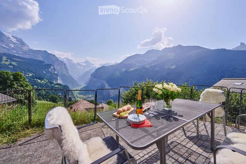 Furniture set on the balcony includes a table, chairs and tableware, overlooking a mountain valley