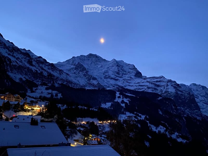 mountain range with snow, moon visible, small town below