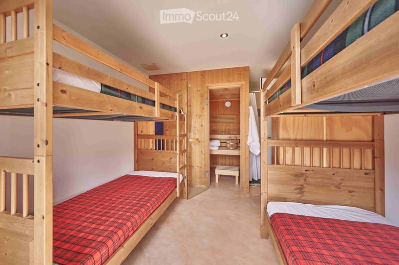 Bedroom with wooden bunk beds, wooden walls, floor, small wooden table and bench, small toilet and shower.