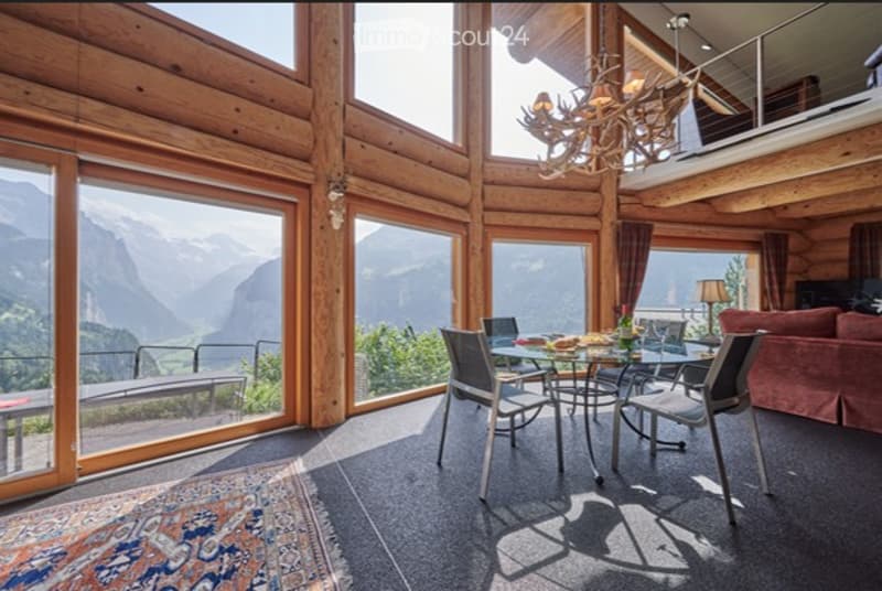 open plan living, dining area with stunning mountain views, wooden interior, glass doors to balcony, large dining table, modern chandelier, cozy couch, lamp
