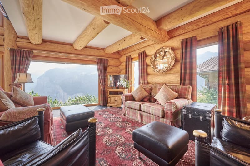 wooden logs on the walls, large windows, red carpet, multiple sofas and armchairs, fireplace