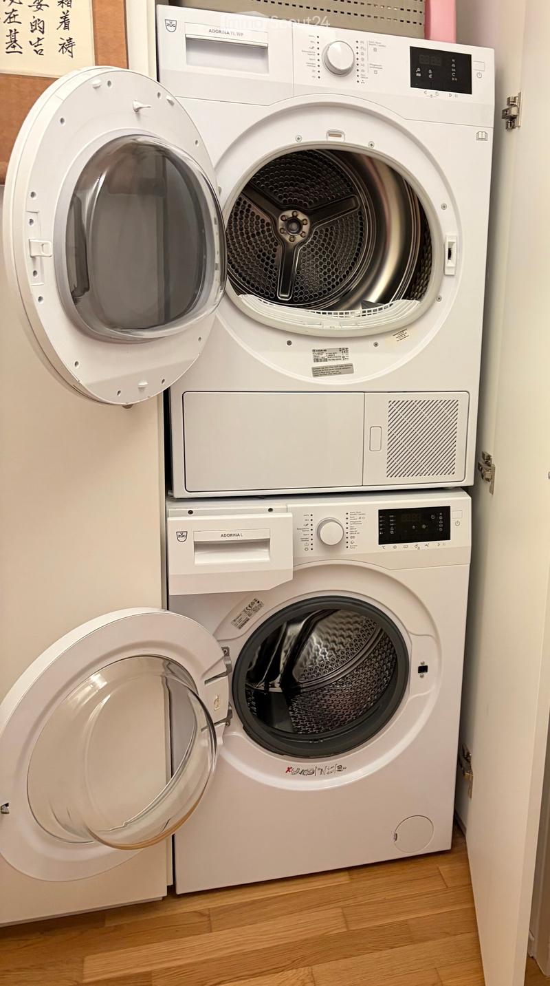 A modern bathroom with a white washing machine and dryer unit, both with open doors showing the interior.