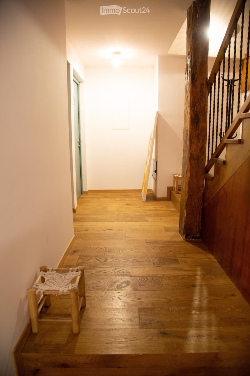 Wooden floor hallway with a staircase featuring a wooden railing and a small woven bench on the left side.