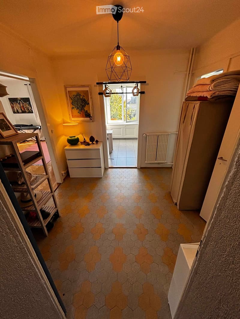 Hallway with hexagonal tile flooring, warm lighting, and a view to an adjacent room with a bed and nightstand.