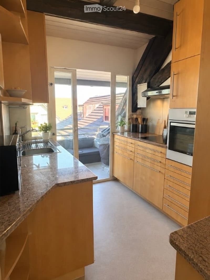 Modern kitchen with light wooden cabinets, granite countertop, stainless steel sink and oven, and a sliding glass door leading to a balcony.