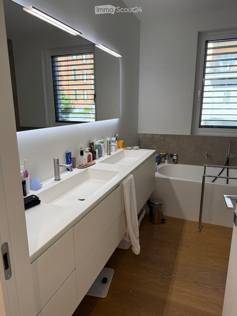 Modern bathroom with double sink vanity, bathtub, large mirror, and wooden flooring.