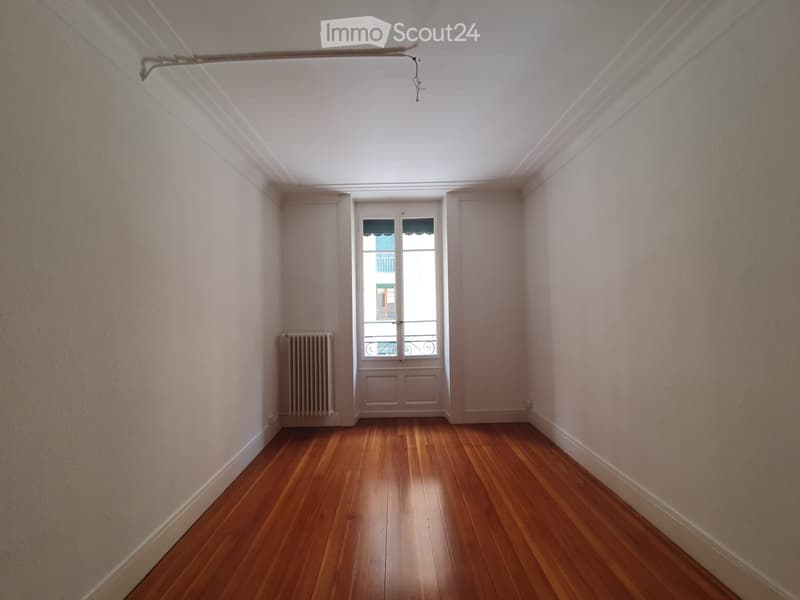 Empty room with wooden flooring, white walls, and a window with a radiator to the left.